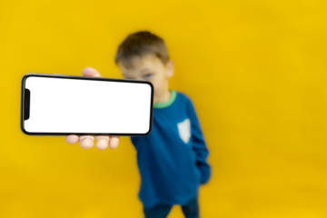 The child holds the phone in his hand for advertising on a yellow background. Color