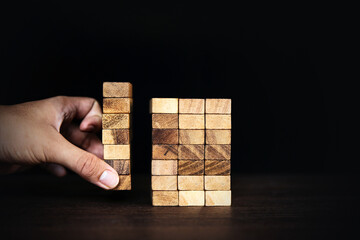 Hand placing wooden block tower stack in pyramid stair step with caution to prevent collapse or...