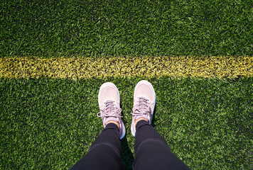 Sports shoes of a woman standing on artificial green grass on a playground behind a line
