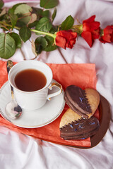 St Valentines breakfast in bed among red traditional roses - vegan heart shaped cookies and coffee cup on the sheets. Aesthetics, romantic lagom holiday background