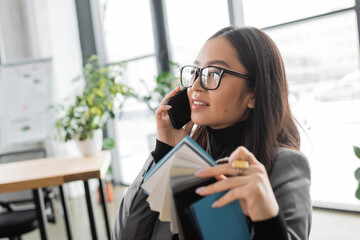 Fototapeta premium Asian designer talking on mobile phone and holding color samples in office.