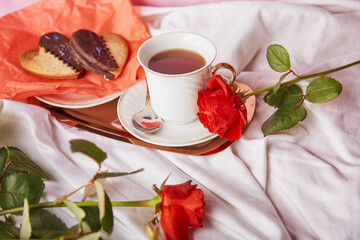 St Valentines breakfast in bed among red traditional roses - vegan heart shaped cookies and coffee cup on the sheets. Aesthetics, romantic lagom holiday background