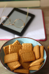 Notebook, pen, tablet, reading glasses, books, phone, candle, bowl of biscuits and cup of tea on the table. Selective focus.