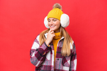 Young beautiful woman wearing winter muffs isolated on red background looking to the side