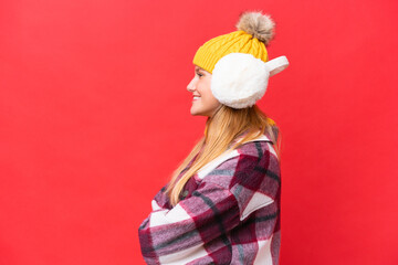 Young beautiful woman wearing winter muffs isolated on red background in lateral position