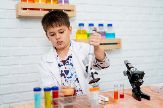 Young boy wear lab gown and action as junior scientist and practice using automatic pipette in science class of the school.