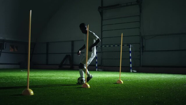 individual training of black football player, man in white uniform running with ball in football pitch