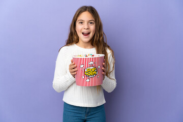 Child over isolated purple background holding a big bucket of popcorns