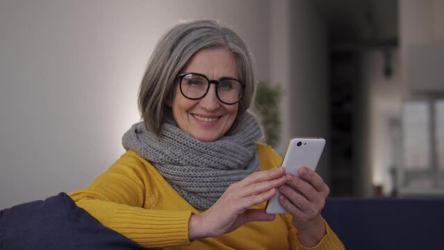 Confident and stylish mature woman receiving additional money working on smartphone from her home, easy income for retired people, advertisement