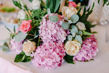 Wedding decor. Festive table decorated with composition of violet, purple, pink flowers and greenery in the banquet hall.