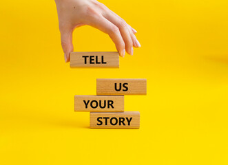 Tell us your story symbol. Concept words Tell us your story on wooden blocks. Beautiful yellow background. Businessman hand. Business and Tell us your story concept. Copy space.