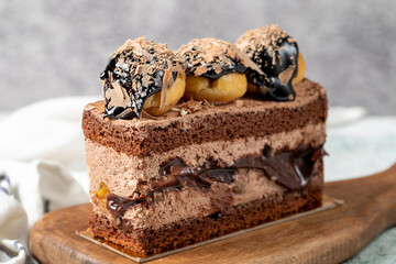 Chocolate and profiteroles cake. Layered cake with chocolate and cream on a wooden serving board on a stone background. close up