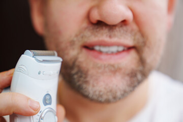 close-up. part of a man's face. a man with bristles holding an electric razor, trimmer. the concept of daily comfortable and safe shaving.