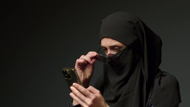 Woman in black muslim headscarf talking on mobile phone. Young arab muslim girl in headscarf hijab using smart phone, close up portrait of smiling middle eastern girl holding mobile smartphone