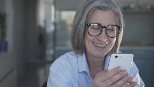 Curious senior woman with stylish gray hair actively typing on smartphone, posting her profile on dating web-site and chatting with men, receiving likes and compliments