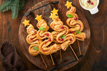 Christmas or New Year appetizer. Christmas tree shape puff pastry buns with cheese and ham. Group of Christmas tree shapes on wooden board. Festive idea for Christmas or New Year dinner. Top view.