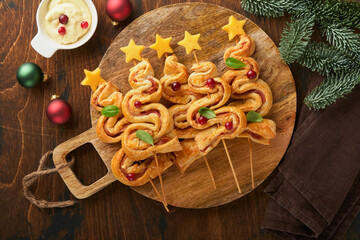 Christmas or New Year appetizer. Christmas tree shape puff pastry buns with cheese and ham. Group of Christmas tree shapes on wooden board. Festive idea for Christmas or New Year dinner. Top view.