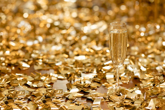 A glass of champagne stands in front of piles of golden coffee on the floor. Holiday concept. Place for text
