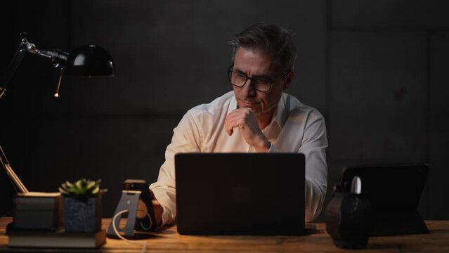 Businessman sitting at desk with laptop computer. Entrepreneur working late in office. Older, middle aged, mid adult, man in his 40s or 50s in business casual.