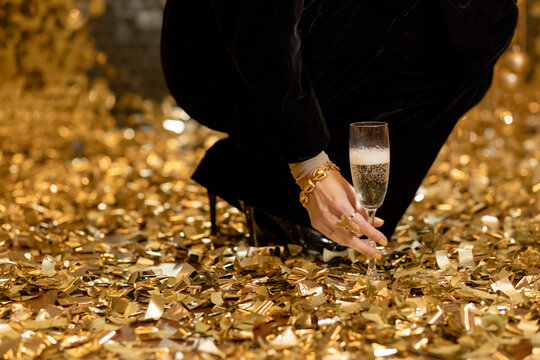 The girl picks up a glass of champagne from the floor amid a pile of golden confetti. Holiday concept. Place for text
