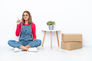 Young caucasian woman sitting on the floor among boxes pointing with the index finger a great idea