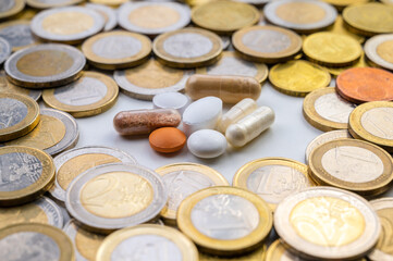 Lozenges and tablets, with coins around them. Costs of medicines, medical therapies and health. Pharmaceutical price increases.
