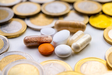 Lozenges and tablets, with coins around them. Costs of medicines, medical therapies and health. Pharmaceutical price increases.
