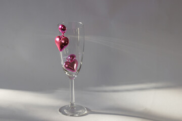 Pair of pink heart shaped earrings on the champagne glass on white background. Romantic jewelry for Valentines party.