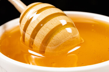 Liquid natural bee honey in a white ceramic bowl with a wooden spoon.