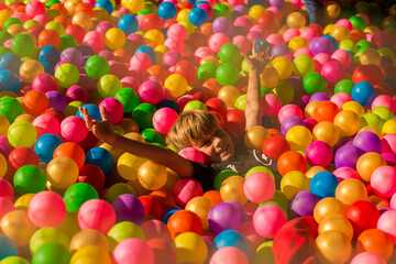 Fototapeta na wymiar Little smiling boy playing lying in colorful balls park playground