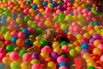 Fototapeta na wymiar Little smiling boy playing lying in colorful balls park playground