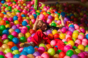 Happy little boy playing and having fun at kindergarten with colorful balls and show thumb up in play center