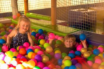 Fototapeta na wymiar Portrait of two funny little kids playing in ball pit and enjoying time in childrens entertainment and play area, copy space