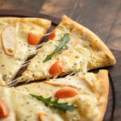 Pizza on wooden board. Slice cut. Hot pizza with melted cheese, chicken, tomatoes and ruccola. Italian food. Serving dish. Wooden background. Close-up. 