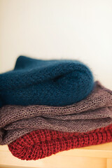 A stack of knitted woolen products lies on a wooden stool