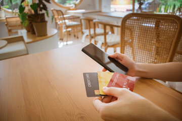 Close up female hands holding smart phone with credit card and choosing to use. using cellphone for...