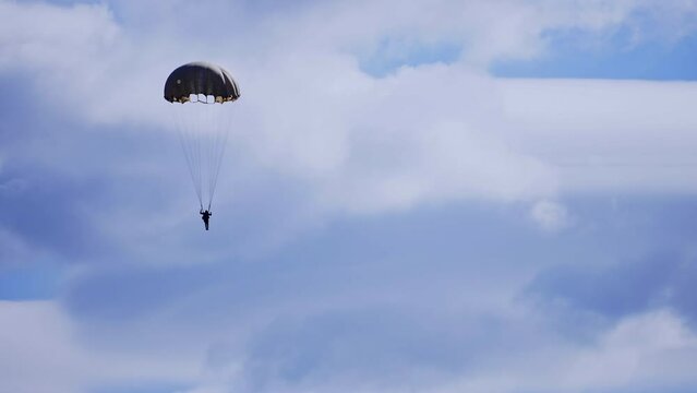 Silhouette of the man with parachute descending to the ground. Parachutist in blue cloudy sky.