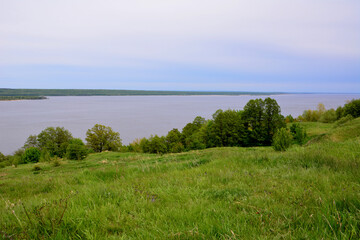 green rolling hill with green trees and Volga river and rainy sky on background