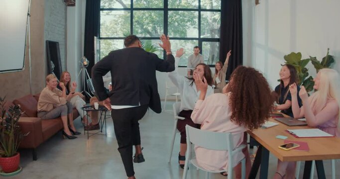 Camera follows African American boss businessman enter office with fun dance celebrating success with team slow motion.