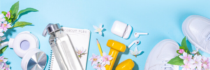 Spring outdoor sport and fitness flat lay. Sport shoes, dumbbells, blank notebook for workout plan, earphones, water bottle on sunny light blue background, top view copy space