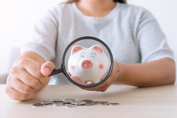 Fototapeta na wymiar Woman using magnifying glass to examine piggy bank concept of financial and money saving