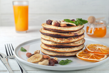 Fresh, delicious pancakes with dried bananas, oranges, nuts and honey on a plate.