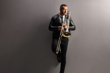 Fototapeta premium Young man with a trombone standing and leaning on a wall