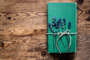 An old green book and lavender flowers, tied with jute twine, on a wooden table. Top view, space for text.
