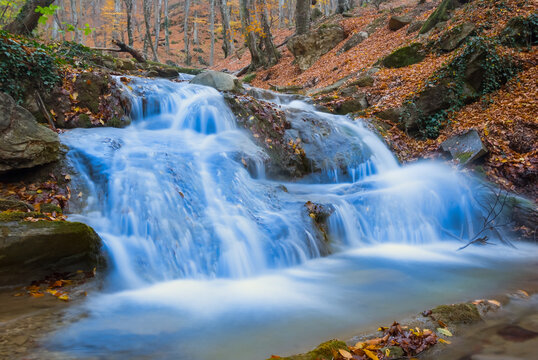 river with waterfall rushing through the mountain canyon among stones and dry leaves © Yuriy Kulik