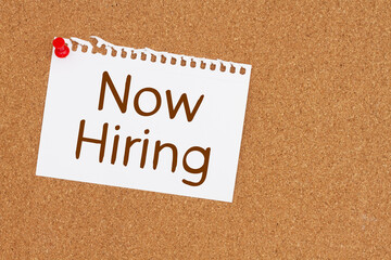 Now hiring message on card on a corkboard