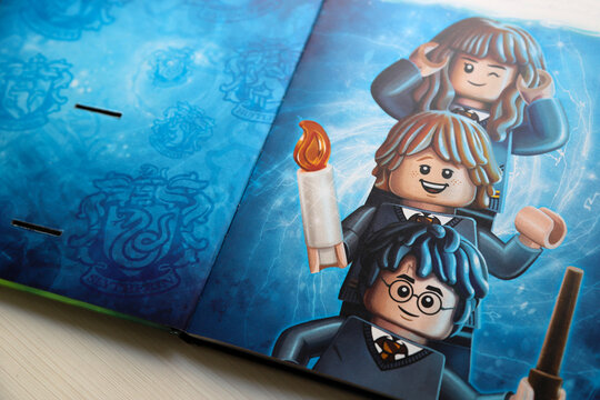  Harry Potter, Ron Weasley and Hermione Granger illustrated with their version of Lego dolls. Book with Lego characters. Illustrated paper book for children. Toys. Hogwarts shield background.