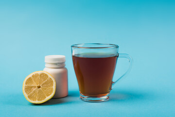 Cup of tea near lemon and pills on blue background.
