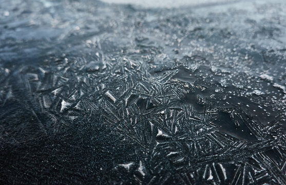 Cracked ice, snowflakes, snow, dark water surface, frozen lake shore. Texture, close-up. Picturesque winter scenery. Concept image, graphic resources. Nature, ecology, climate change, global warming
