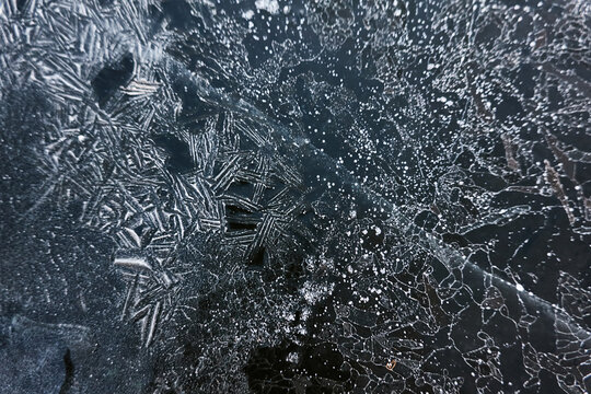 Cracked ice, snowflakes, snow, dark water surface, frozen lake shore. Texture, close-up. Picturesque winter scenery. Concept image, graphic resources. Nature, ecology, climate change, global warming